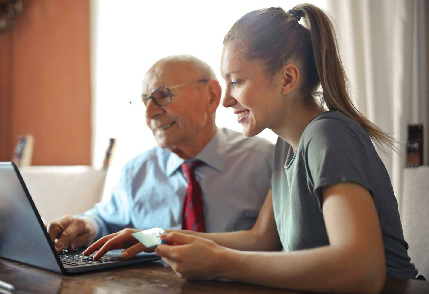 Young woman and elderly man working together on a laptop computer.