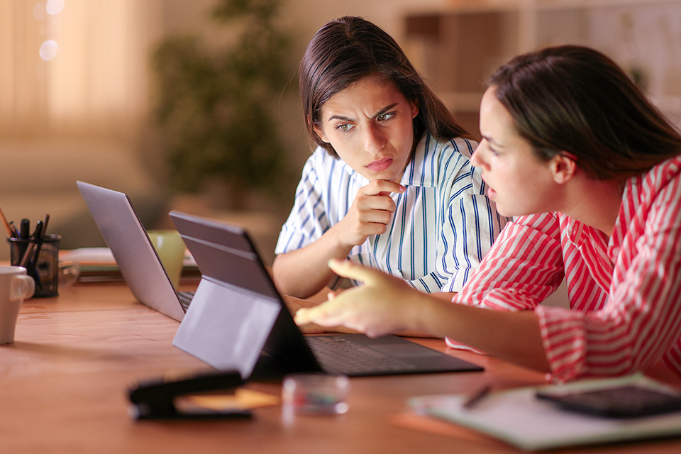 Two women studying a computer screen with look of confusion and concern.